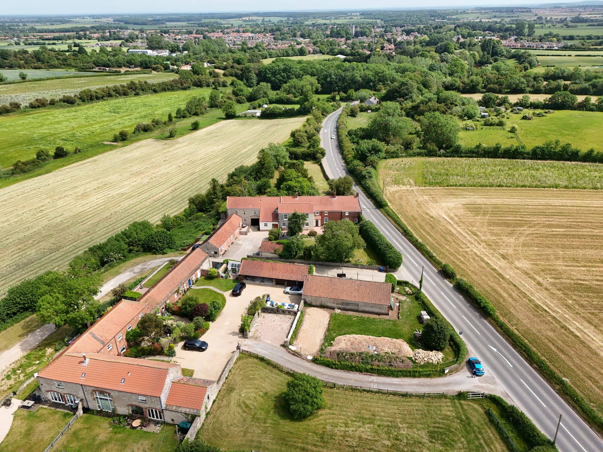 Aerial view of a farmhouse beside a road running through open countryside